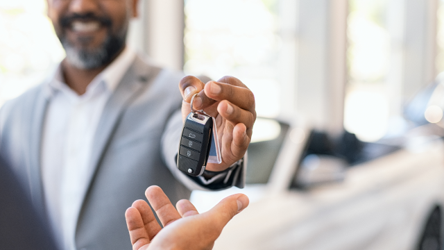 A car salesman hands a car key to another person.