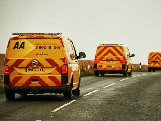 Yellow AA patrols on a remote country road Three yellow AA patrol vans drive down a remote country road
