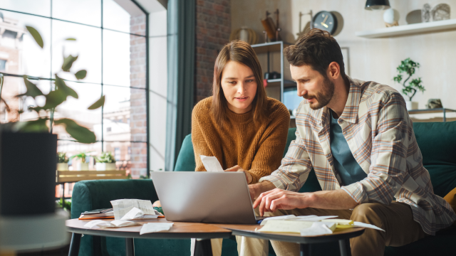 A man and a woman sort through paperwork, with a laptop open in front of them.